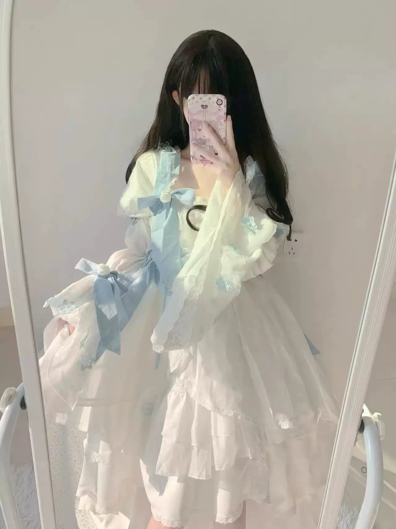 White Lolita one-piece dress with pale blue bows and layered lace ruffles shown in a mirror selfie.