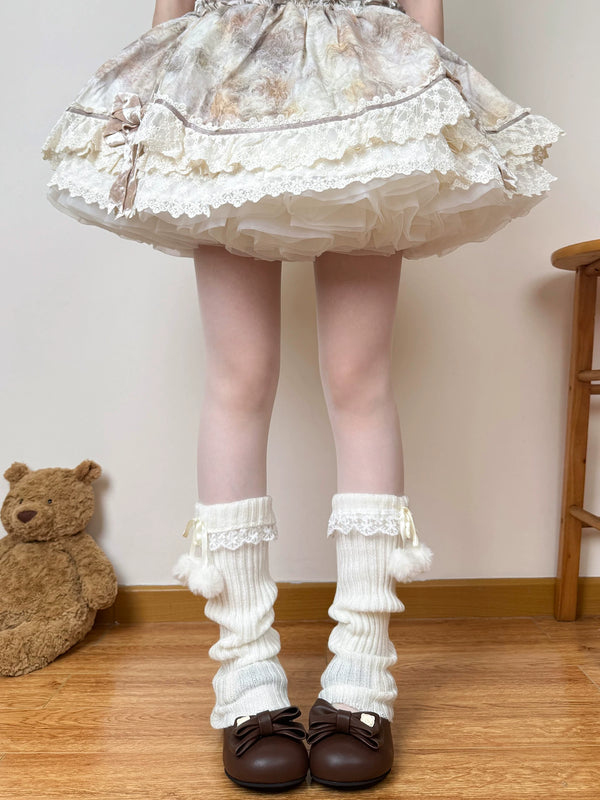 White scrunched leg warmers with lace cuffs and pom-pom ties worn with a pale skirt