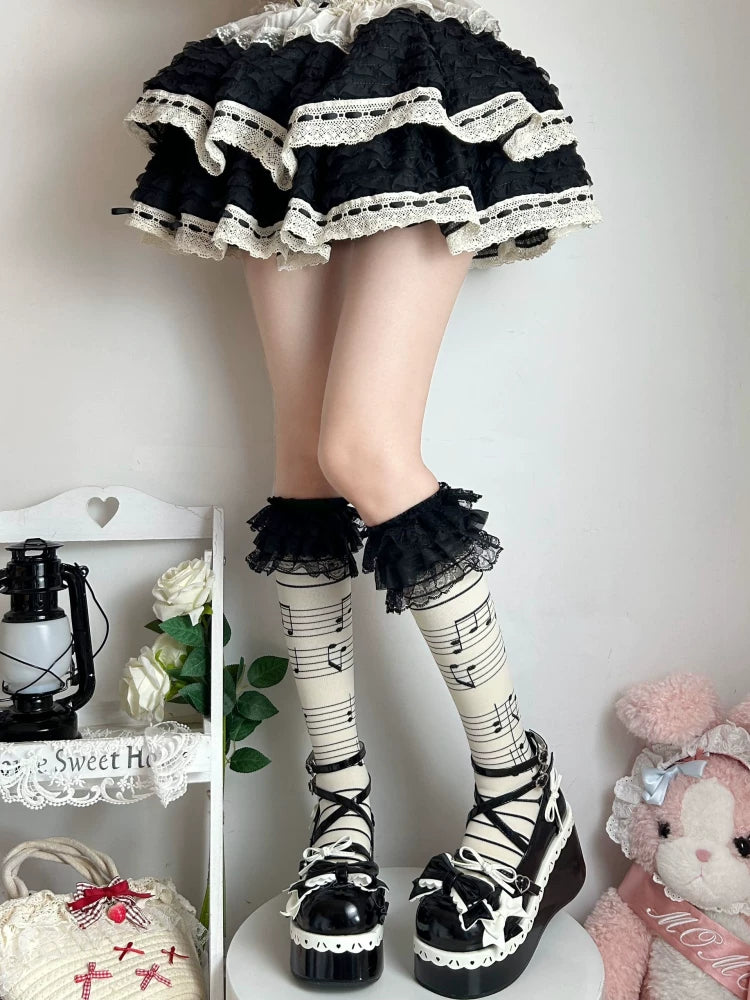 Light musical-note socks with black lace ruffle cuffs styled beneath a black skirt.