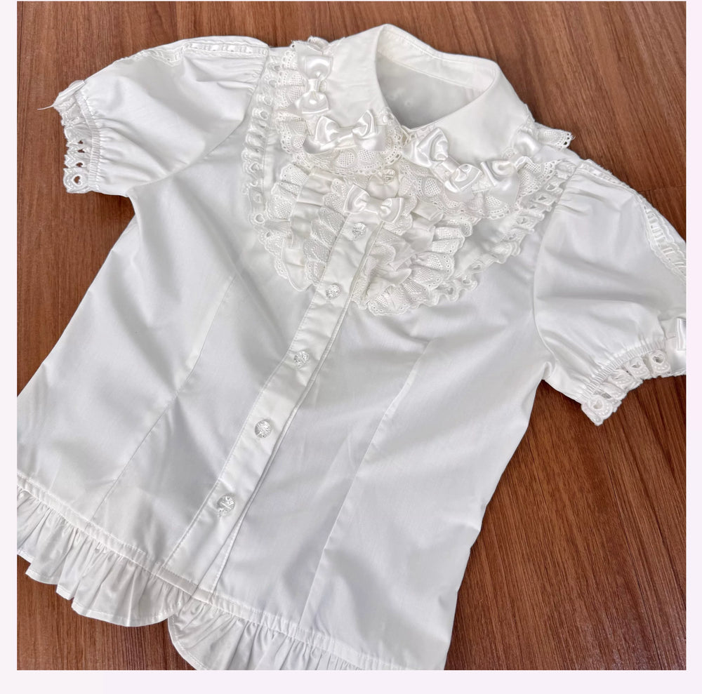 White short-sleeve blouse with lace doll collar, bows and ruffled hem laid flat