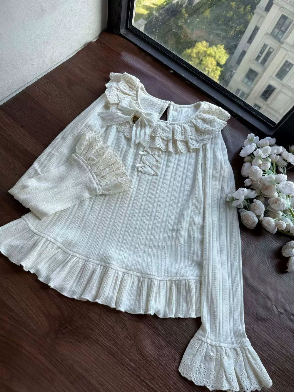 White ribbed knit layering top with ruffled lace collar and flared cuffs on a hanger