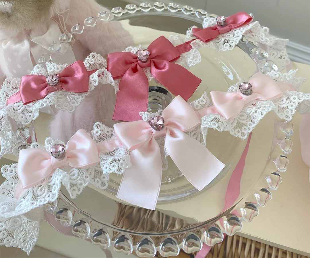 Pink and white lace chokers with oversized satin bows displayed on a mirrored tray.