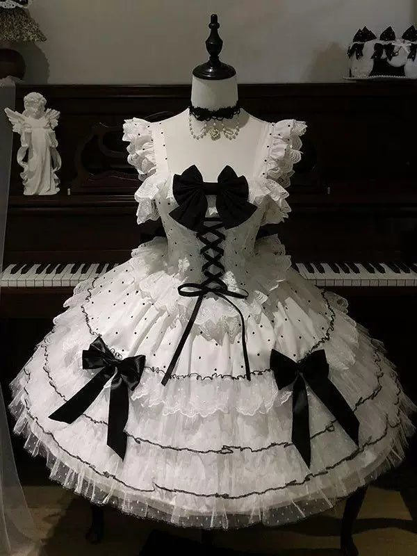 White and black JSK dresses with contrast bows, front lacing and tiered ruffle skirts displayed on dress forms.