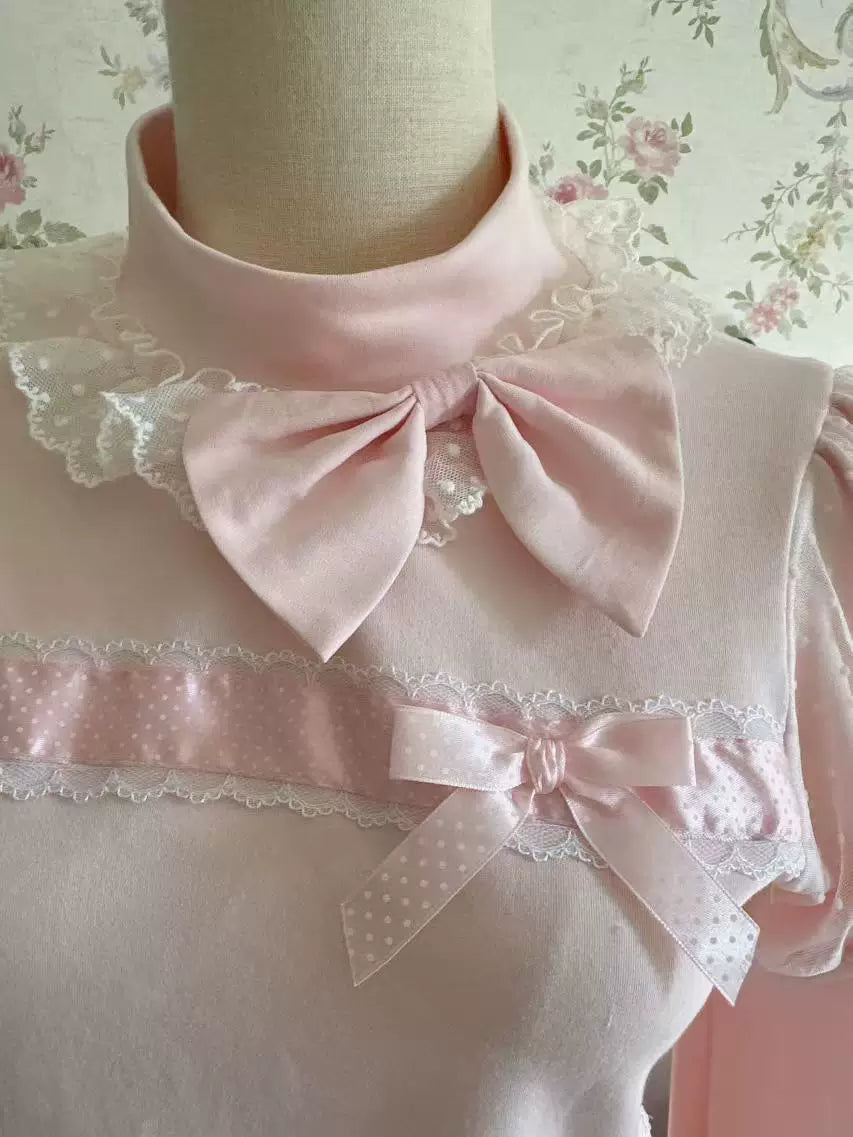 White long-sleeve inner top with lace ruffles, a pink bow and bead chain laid on a wood floor.