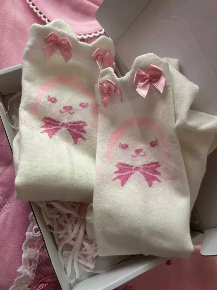 White over-the-knee socks with repeating pink bunny faces and bows, shown flat in their packaging.