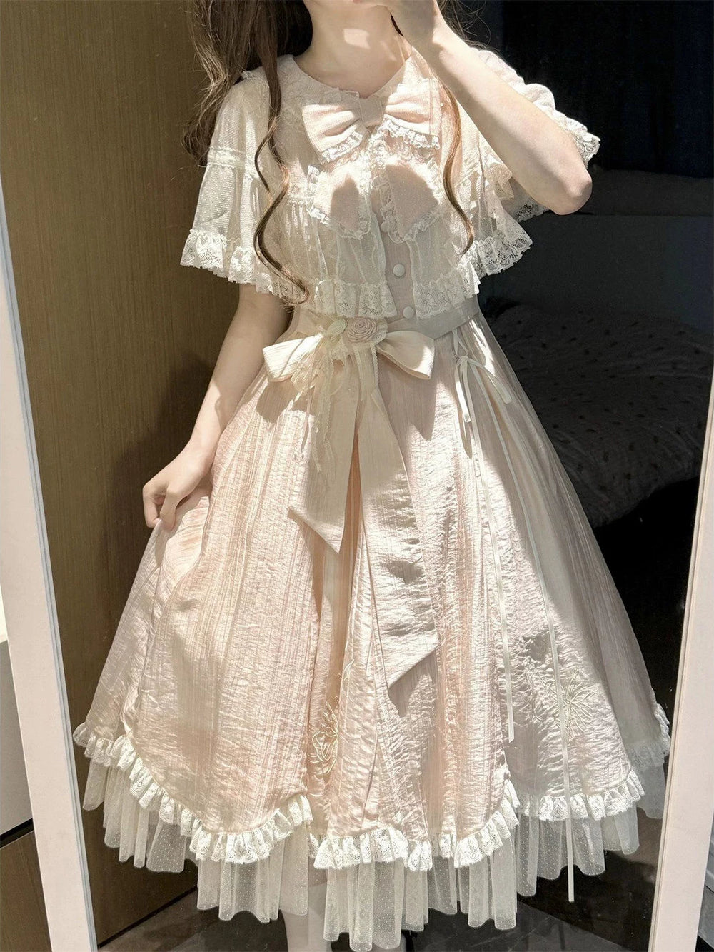 Pink lace-trimmed one-piece dress with cape overlay, bows, ribbon lacing, and layered hem.