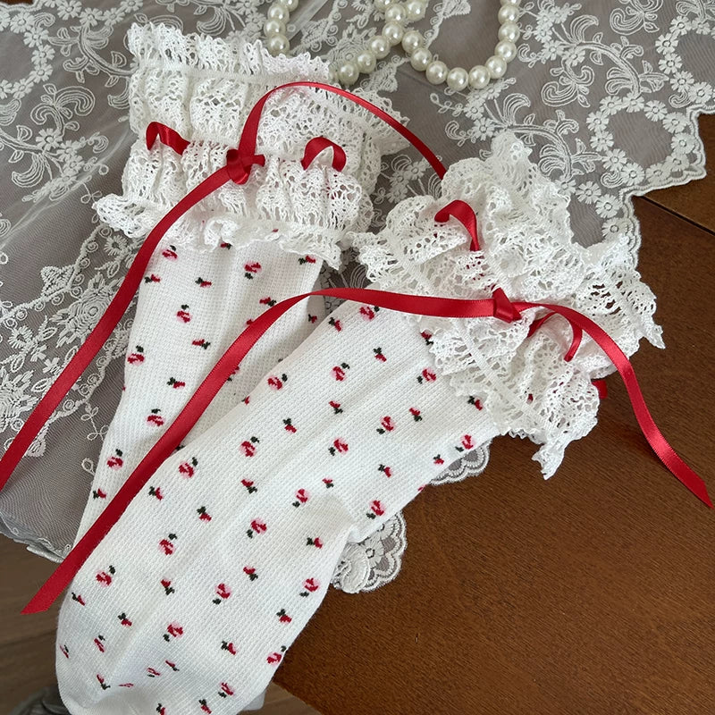 White mid-calf socks with tiny red motifs, wide lace cuffs and red ribbon ties.