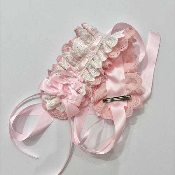 Pink-and-white lace headband with layered bows and trailing ribbon ties shown flat.