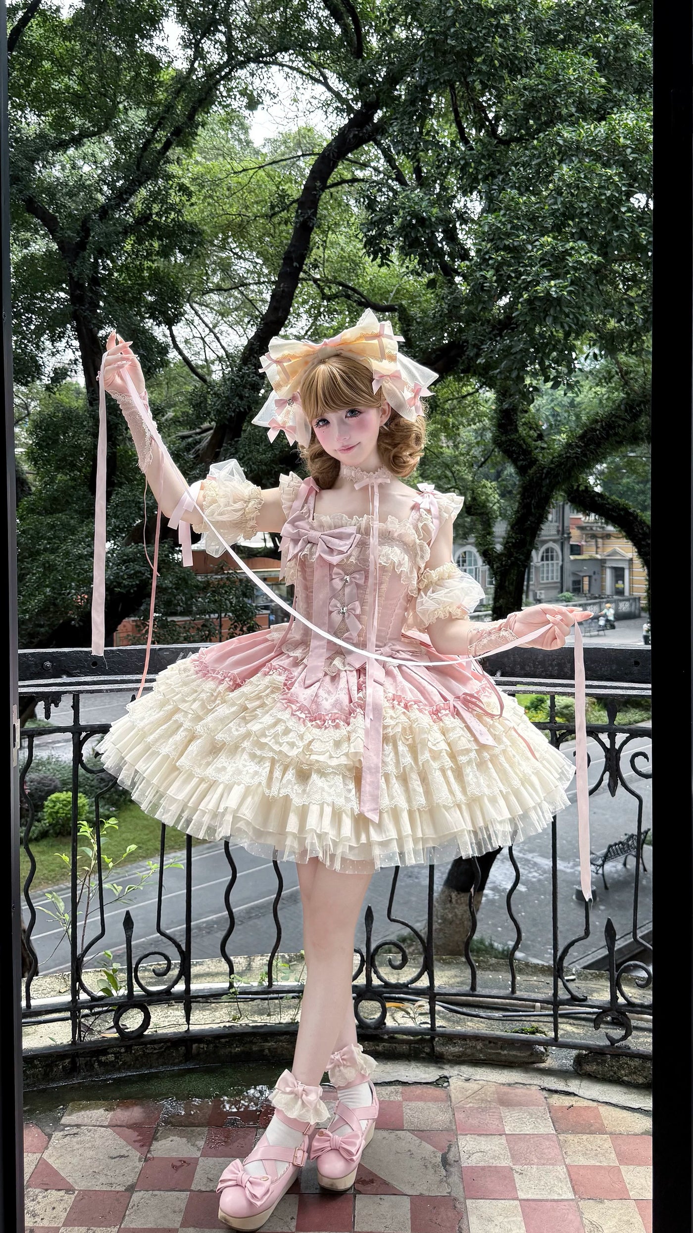 Pink and cream ruffled JSK dress with layered lace and repeated bows worn outdoors.