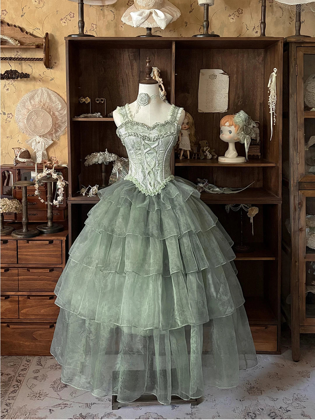 Muted green dress on a mannequin with a lace-up bodice, scalloped lace and tiered skirt.