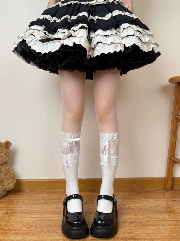Black and white lace-trimmed Lolita socks with ribbon ties worn beneath a tiered black skirt and Mary Jane shoes.