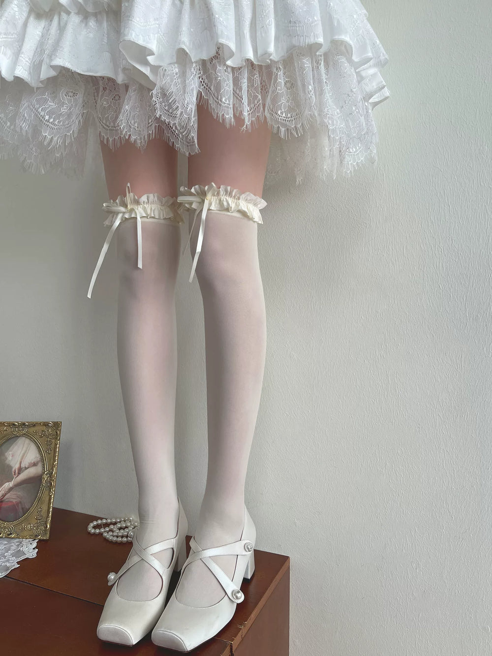 White over-the-knee socks with ruffled bow cuffs beneath a lace-trimmed skirt