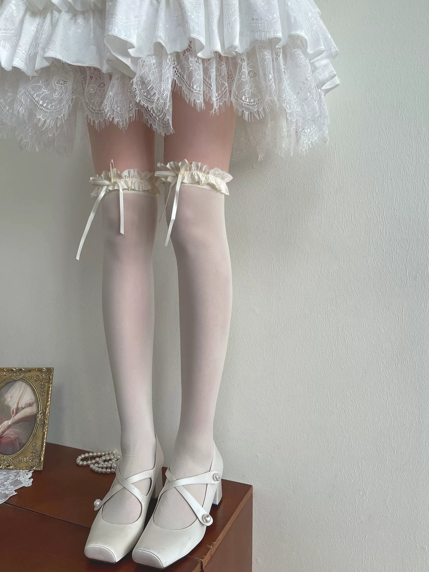 White over-the-knee socks with ruffled bow cuffs beneath a lace-trimmed skirt