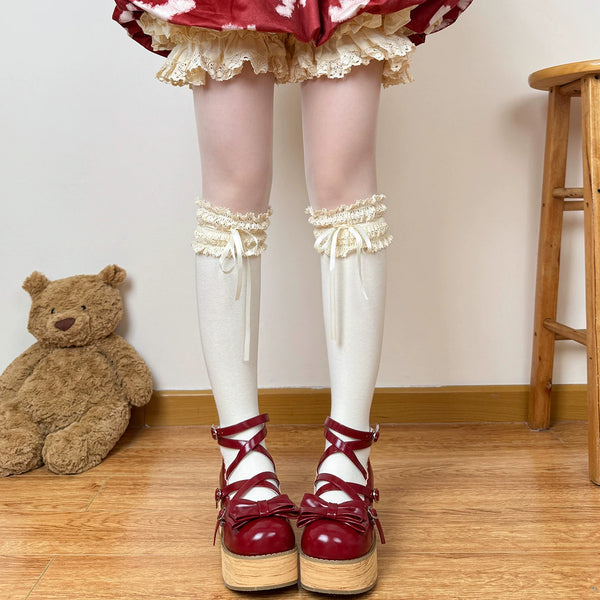 White socks with layered lace cuffs and ribbon ties styled beneath a vintage doll dress.
