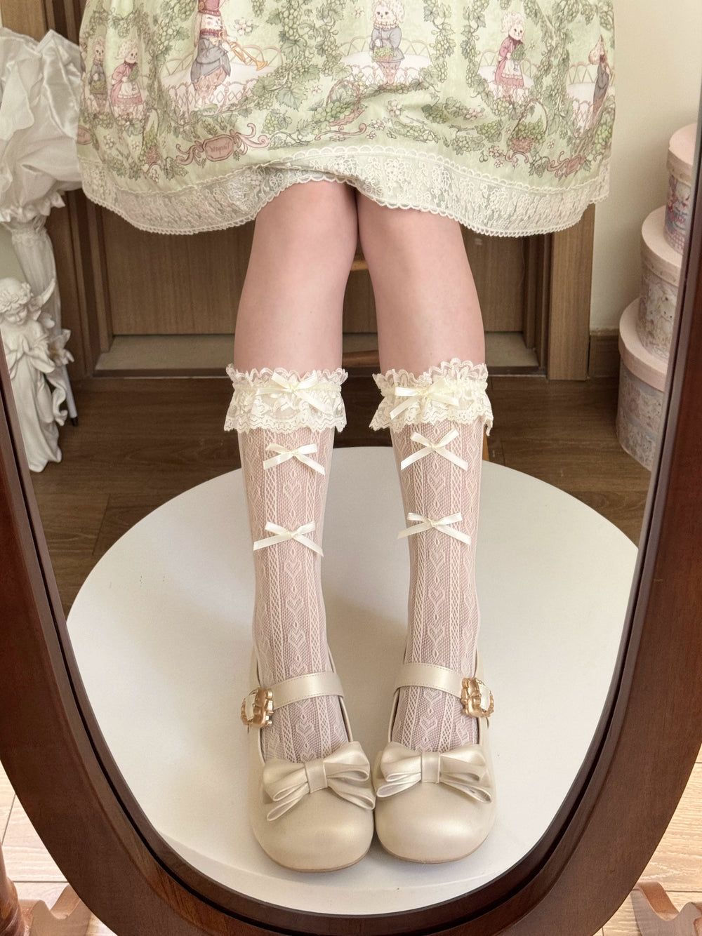 Yellow patterned lace mid-calf socks with cream bows and ruffled cuffs styled with a pale Lolita skirt.