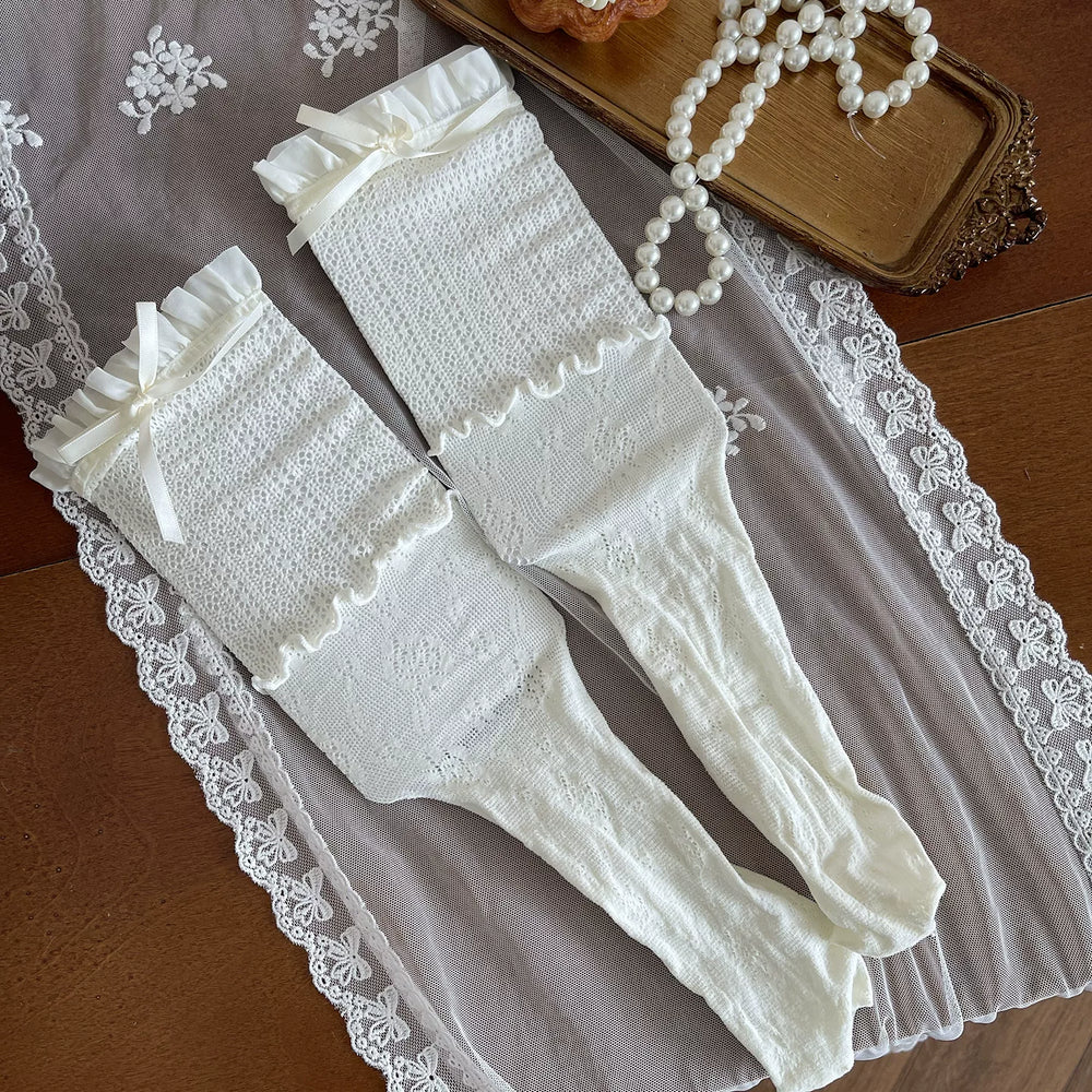Cream and white layered lace hosiery with bows and fishnet panels styled on a model.