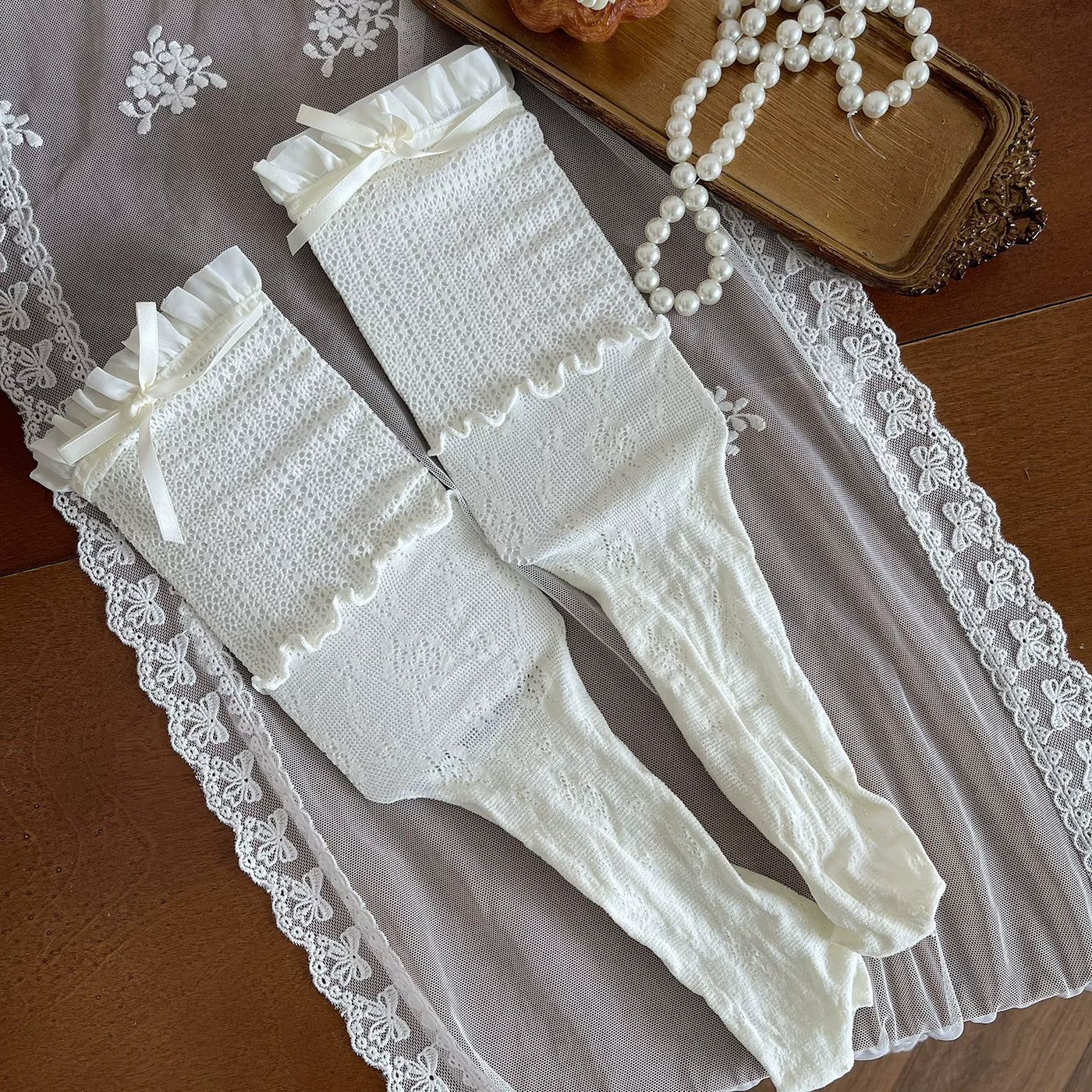 Cream and white layered lace hosiery with bows and fishnet panels styled on a model.