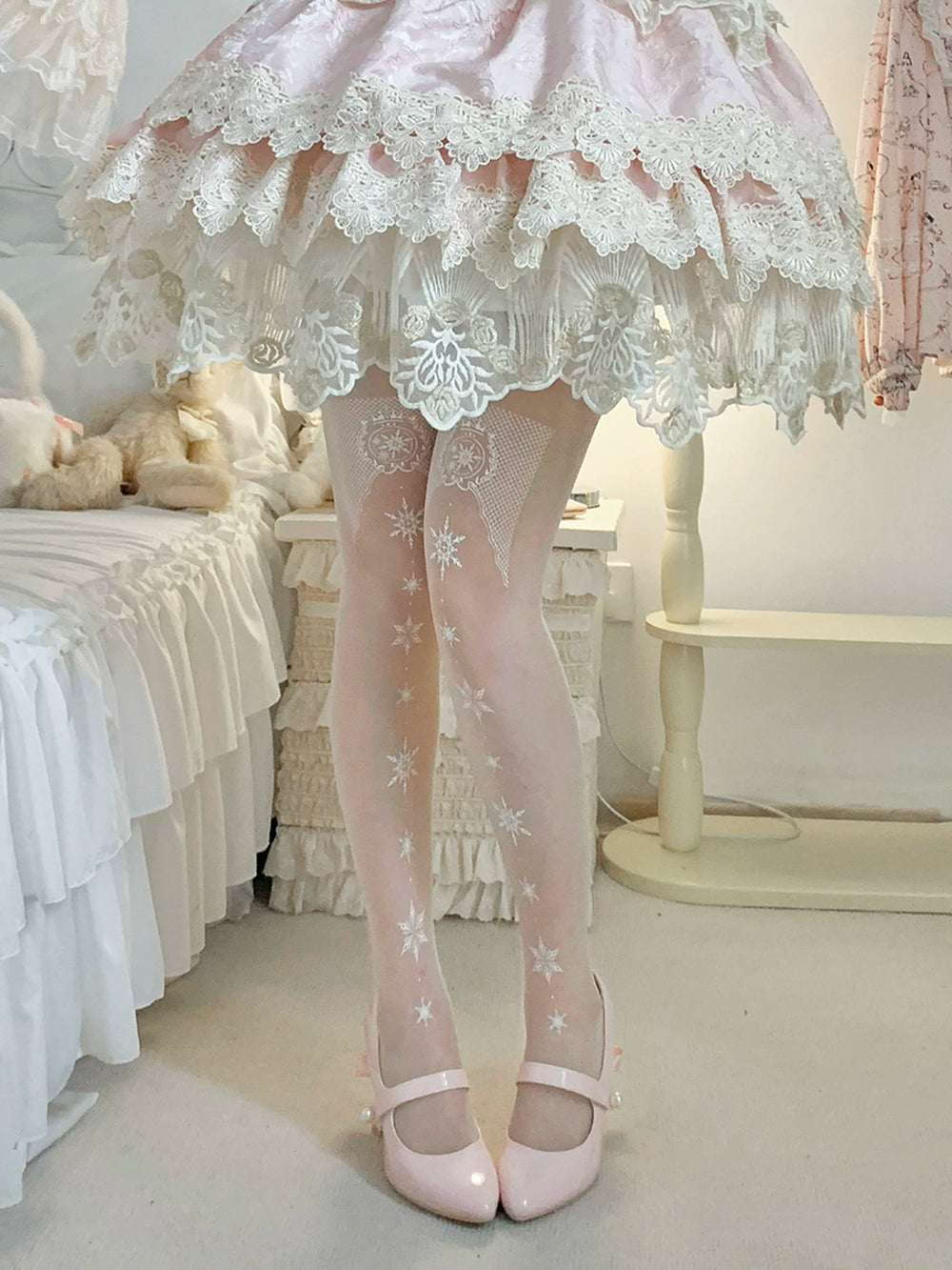 Model wearing pale pantyhose with repeated white snowflake motifs beneath a pink lace-trimmed skirt.