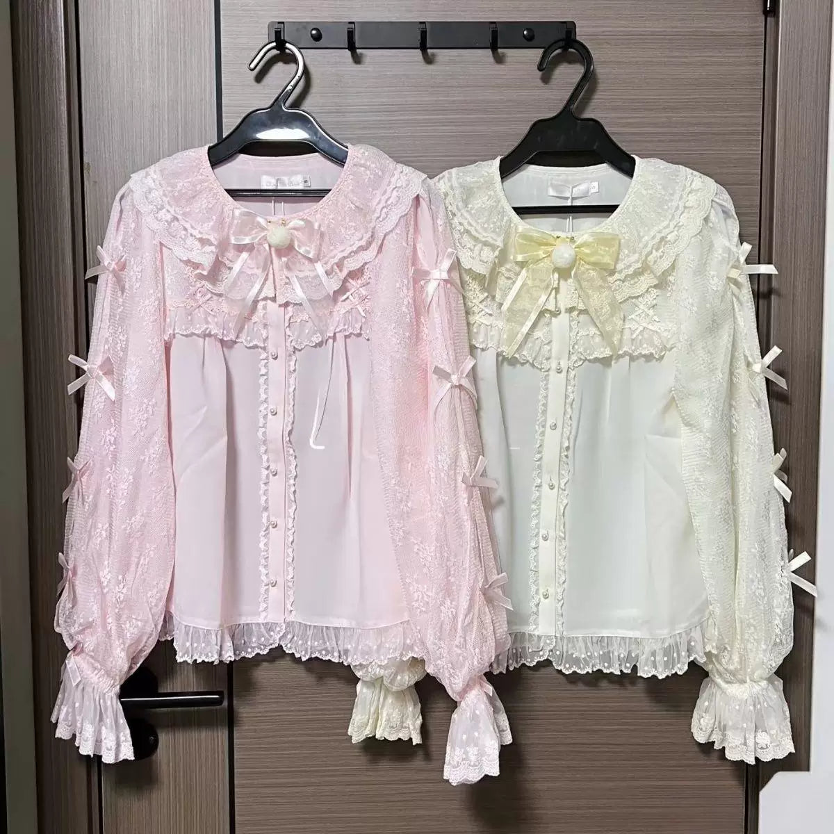 Pink lace blouse displayed on a hanger with layered bows and ruffled details.
