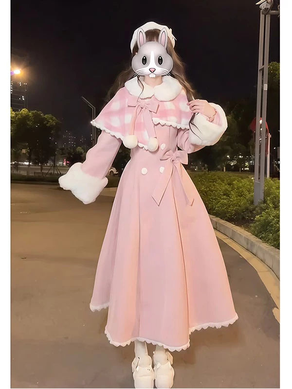 Model in a pink long coat with a pink plaid cape and white trim outdoors at night.