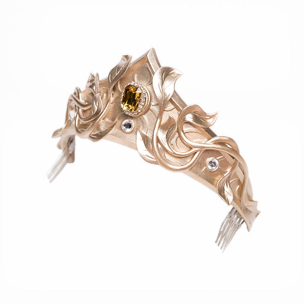 Jeweled gold-tone crown accessory with leaf-like filigree and a central amber-colored stone.