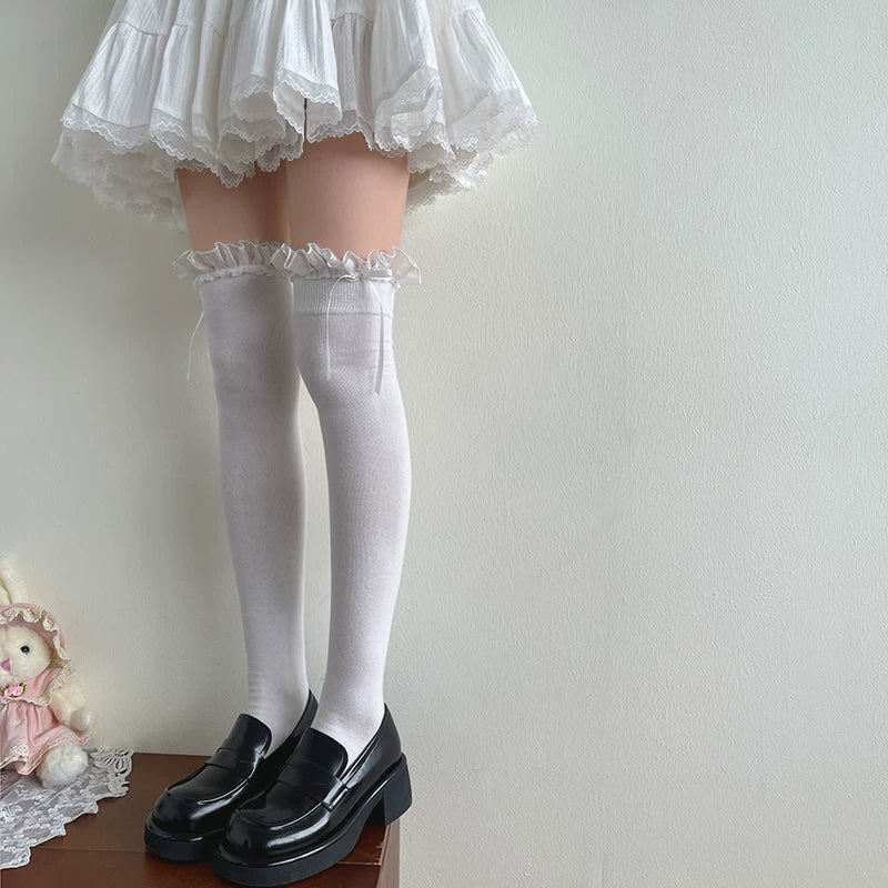 White thigh-high socks with ruffled lace cuffs and bow ties styled with black shoes.