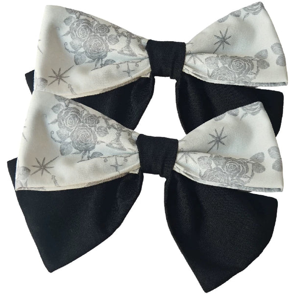 Pair of black and cream bow hairclips with rose and cross print panels.
