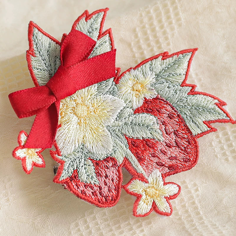 Strawberry embroidered brooch with a red bow on white lace