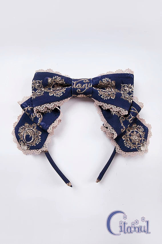 Navy ornate bow headband with lace edging and framed print on a white background.
