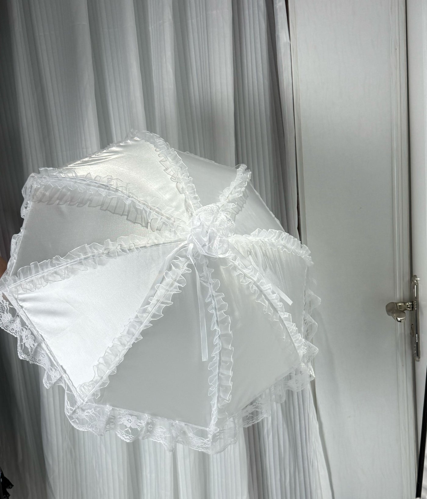 White lace-trimmed parasol with ribbon details held in a mirror photograph.