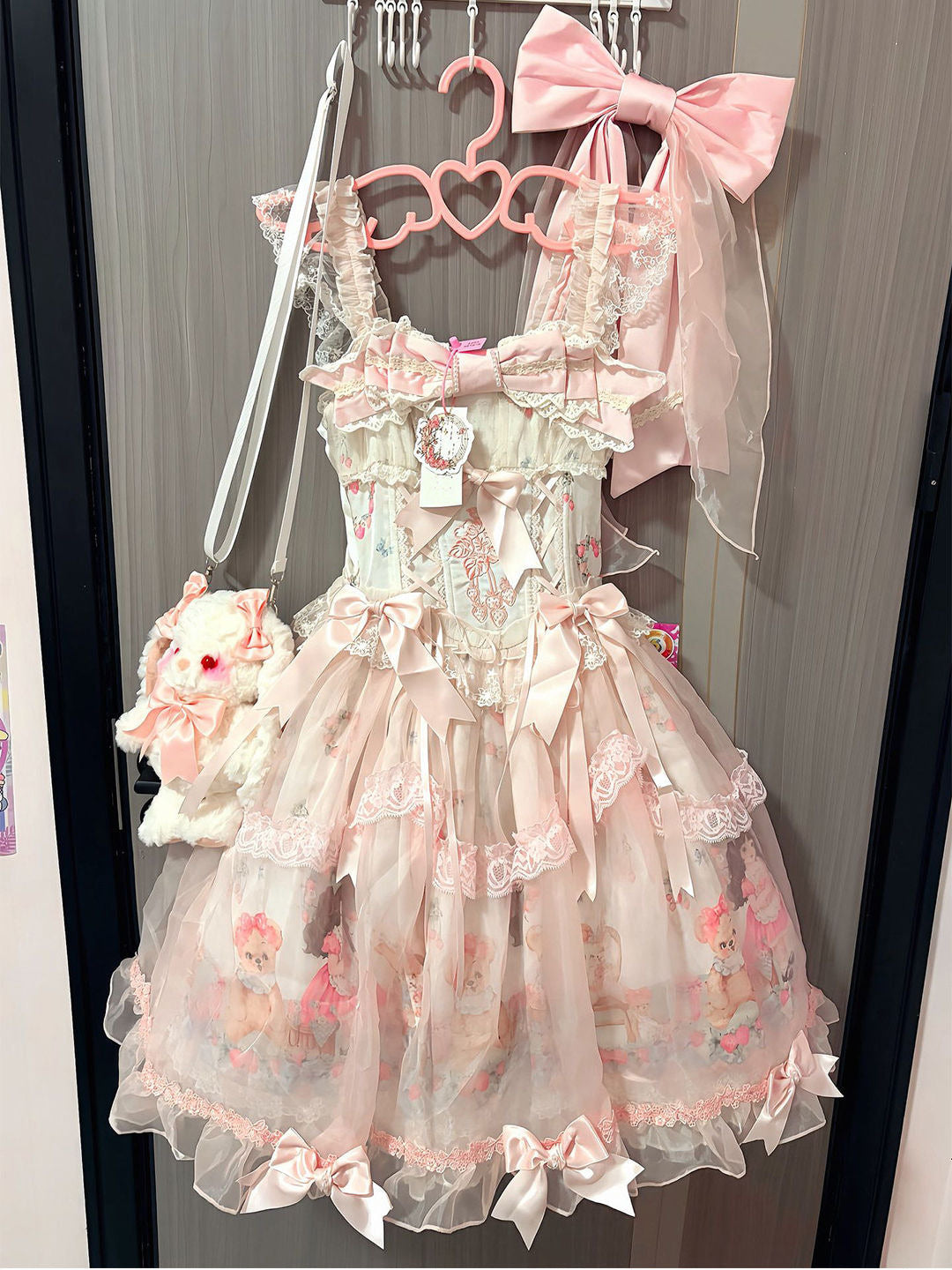 Pink and cream bear-print bow dress hanging on a heart-shaped hanger.