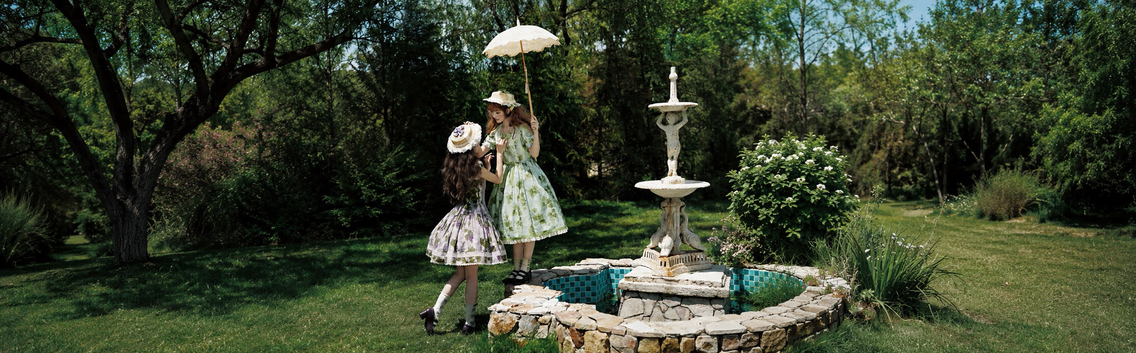 Two Lolita models wearing light summer dresses beside a garden fountain.